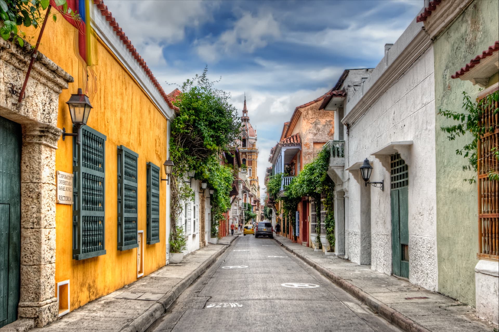 Calle del centro histórico de Cartagena con casas amarillas y blancas y una torre de iglesia al fondo