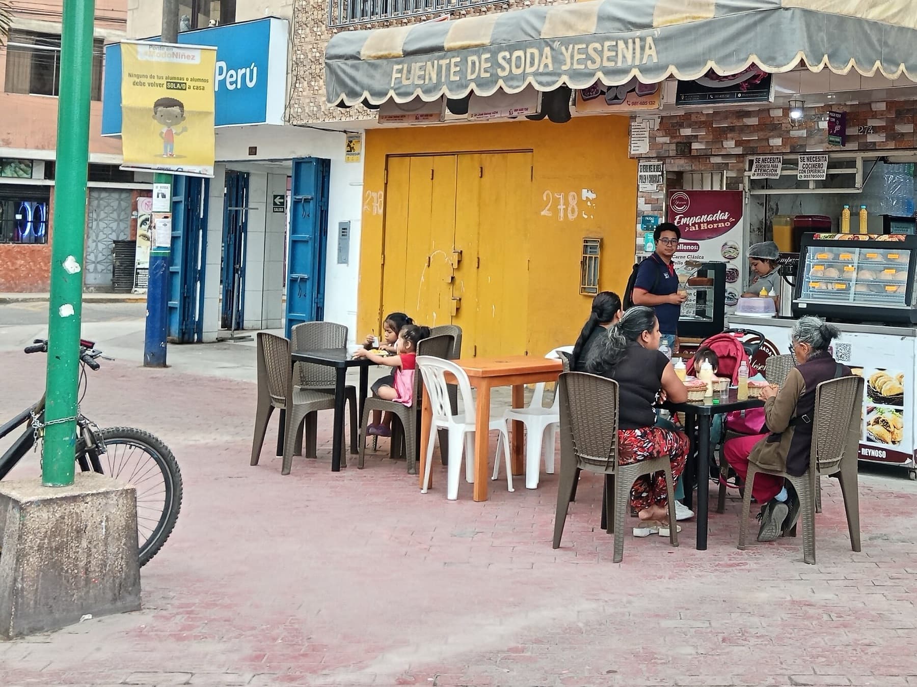 Una fuente de soda de barrio con mesas en la acera y clientes sentados